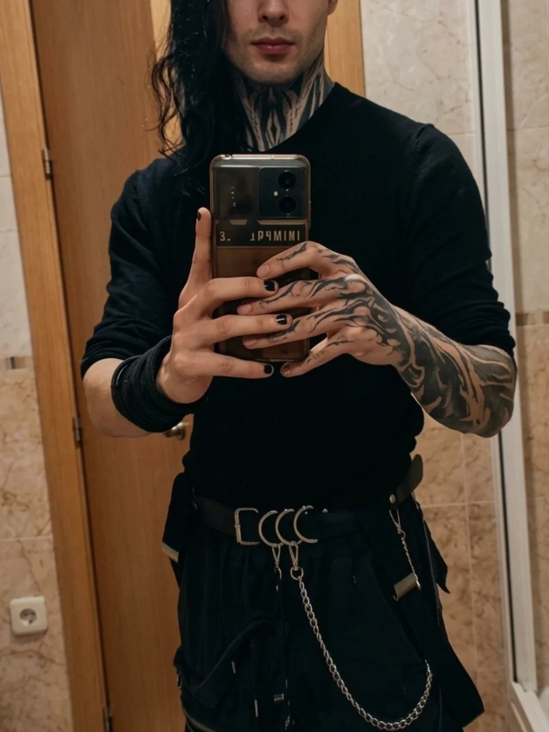 Man in black long-sleeved shirt and chain belt posing for a mirror selfie.