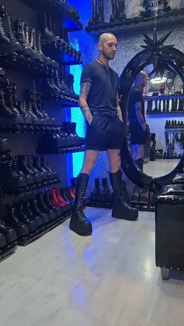 Man wearing tall platform black combat boots in a gothic footwear store.