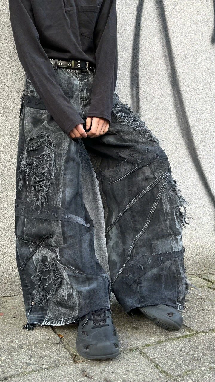 Person in oversized distressed grey denim trousers and black shirt against graffiti wall