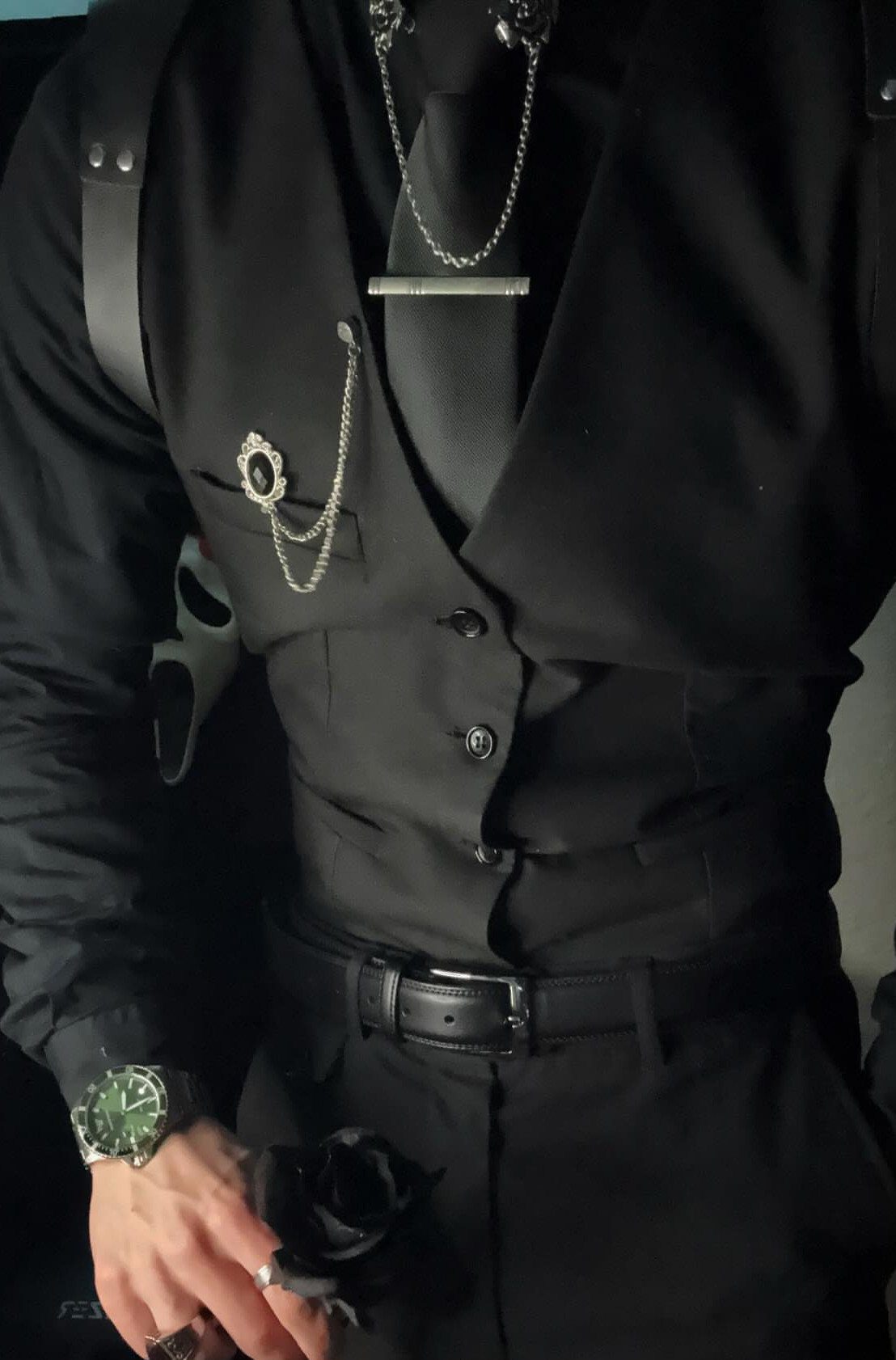 Man in a formal black gothic vest, tie, and silver jewelry accessories.