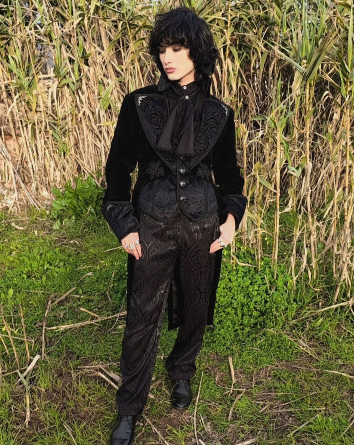 Person wearing a black luxe velvet long coat and matching gothic ensemble in grass.