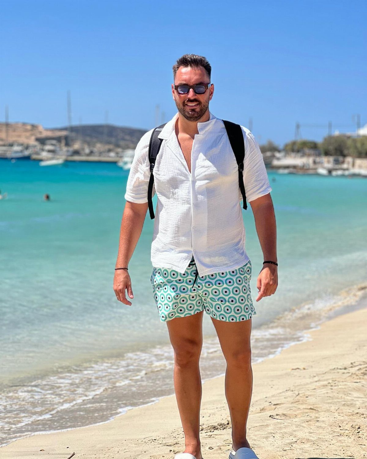Man in white button-down shirt and patterned swim shorts on a sunny beach