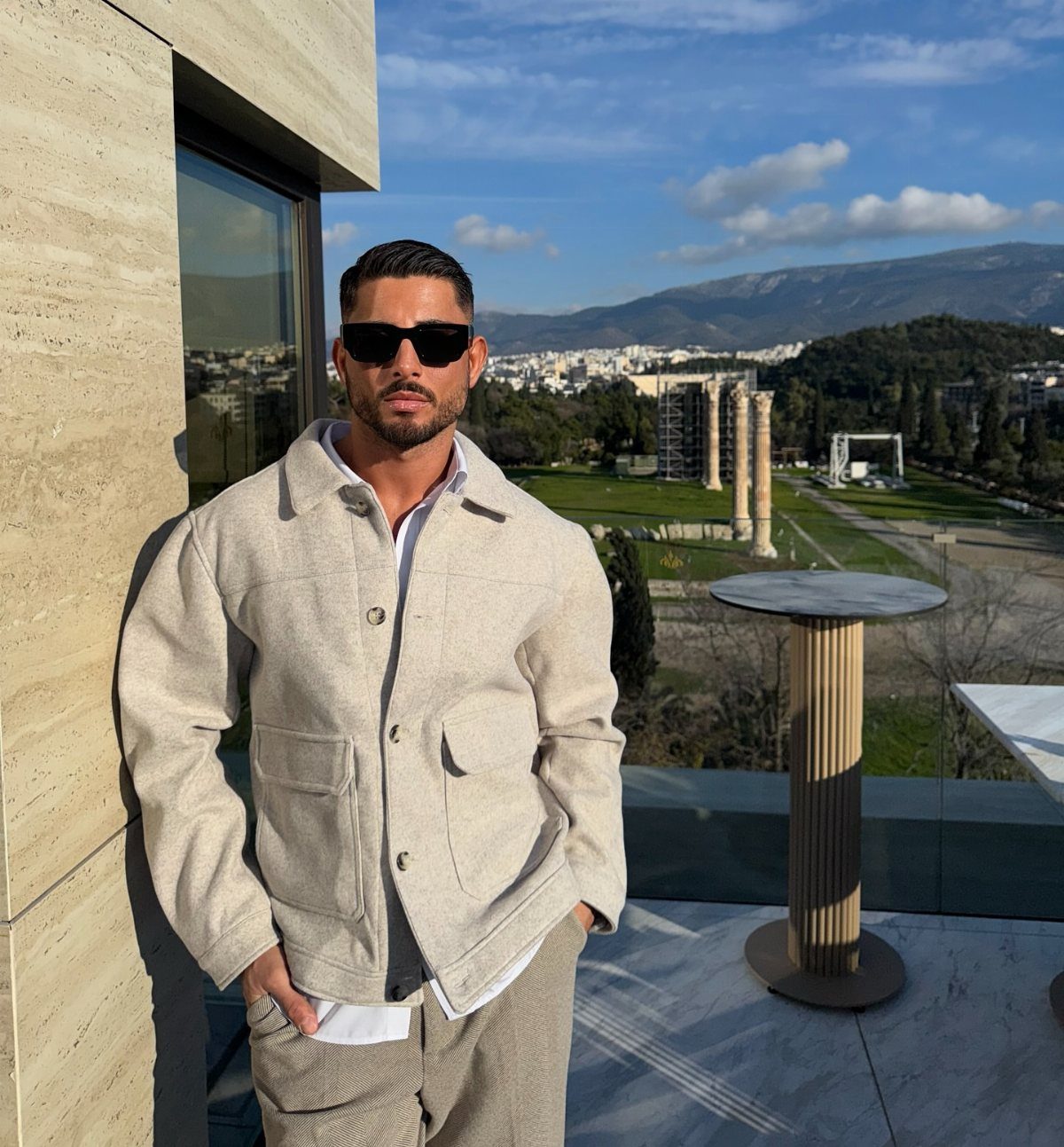 Man in beige overshirt jacket and trousers posing on a balcony in Greece