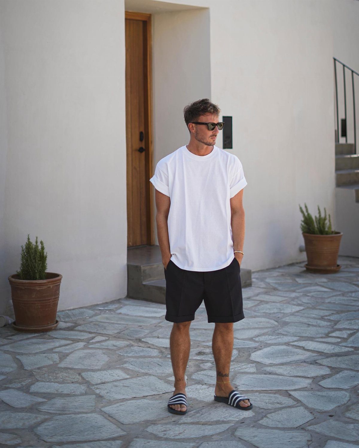Man wearing white t-shirt and black shorts standing on stone pavement in Greece.