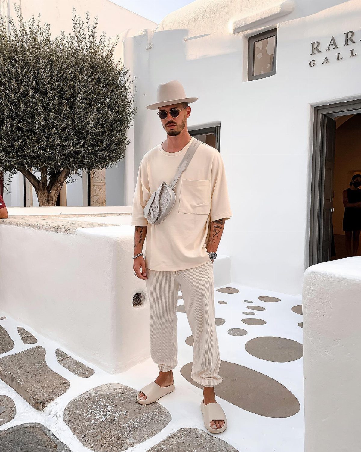 Man in beige t-shirt and ribbed trousers wearing slide sandals in Greece.