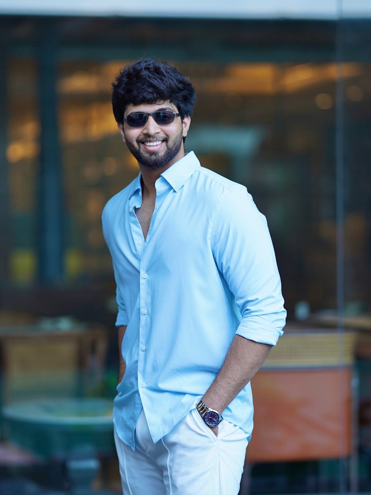 Smiling man with groomed facial hair wearing a light blue shirt and sunglasses.
