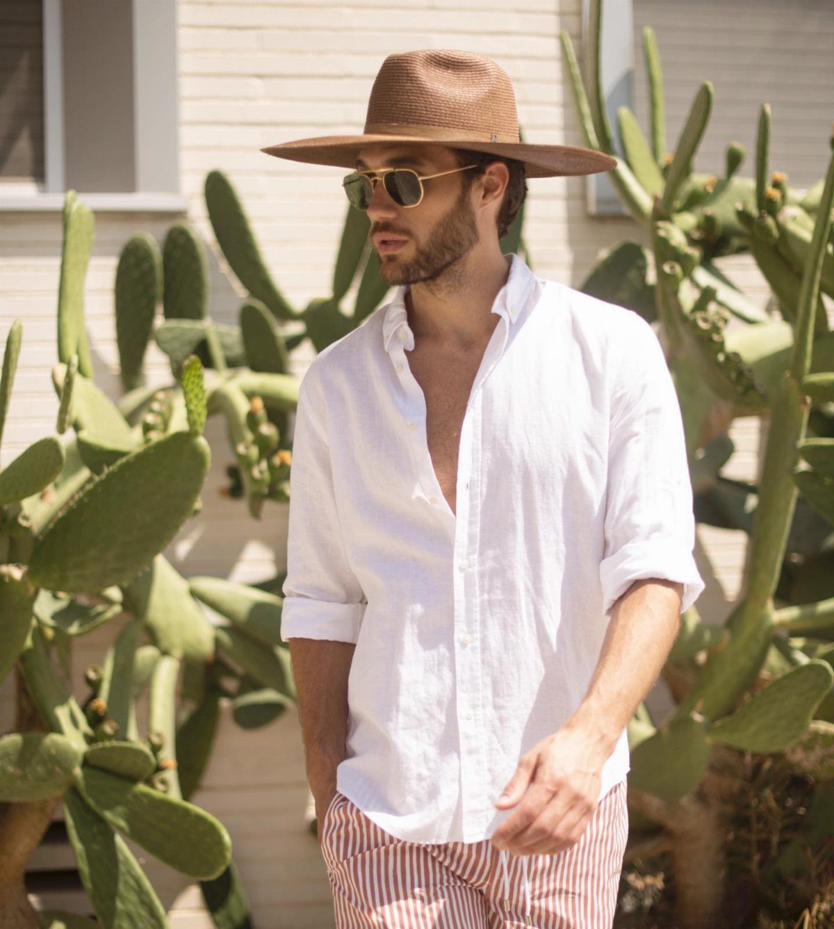 Man in a brown straw hat and white linen shirt posing by cacti.