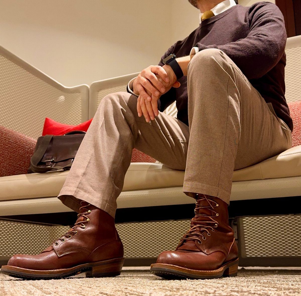Man wearing brown leather lace-up boots and tan trousers sitting on a white sofa.