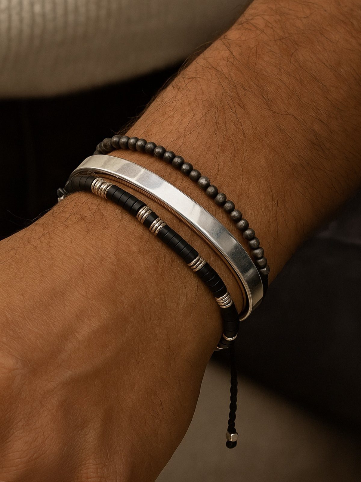 Three men's bracelets including a silver cuff and beaded bands on a wrist.