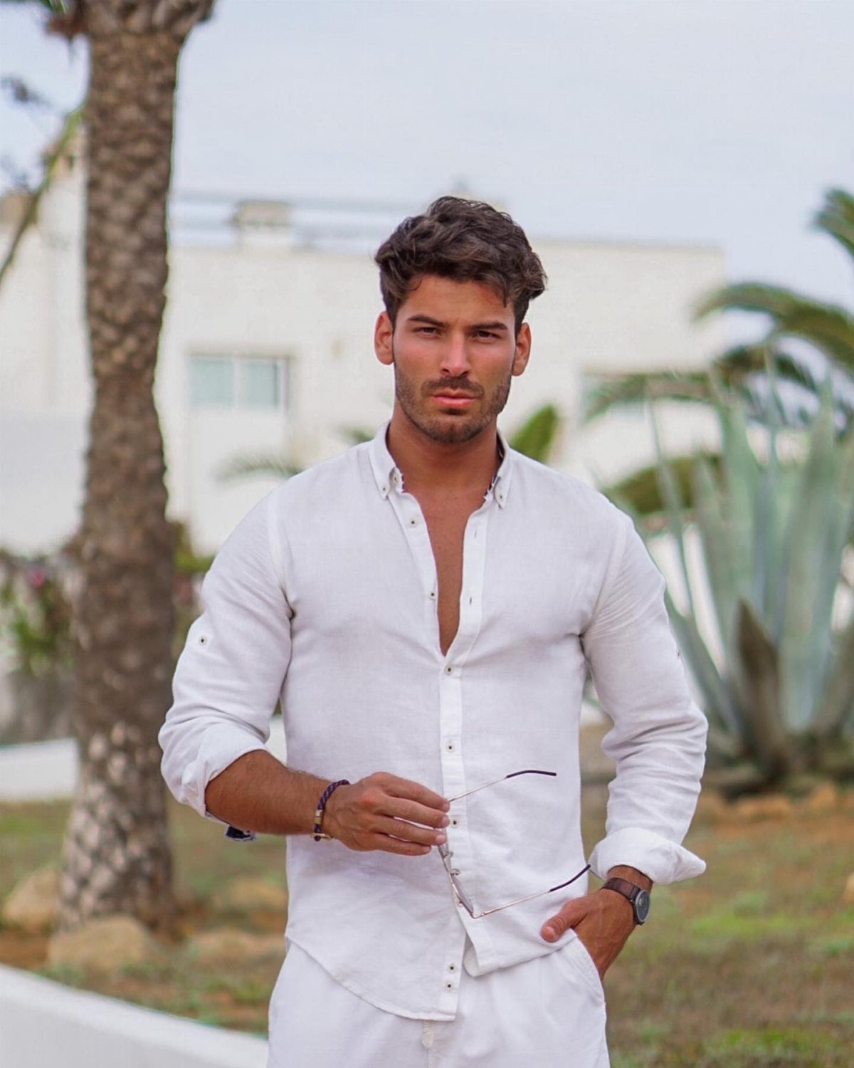 Man wearing a white linen shirt and white trousers in a sunny outdoor setting.