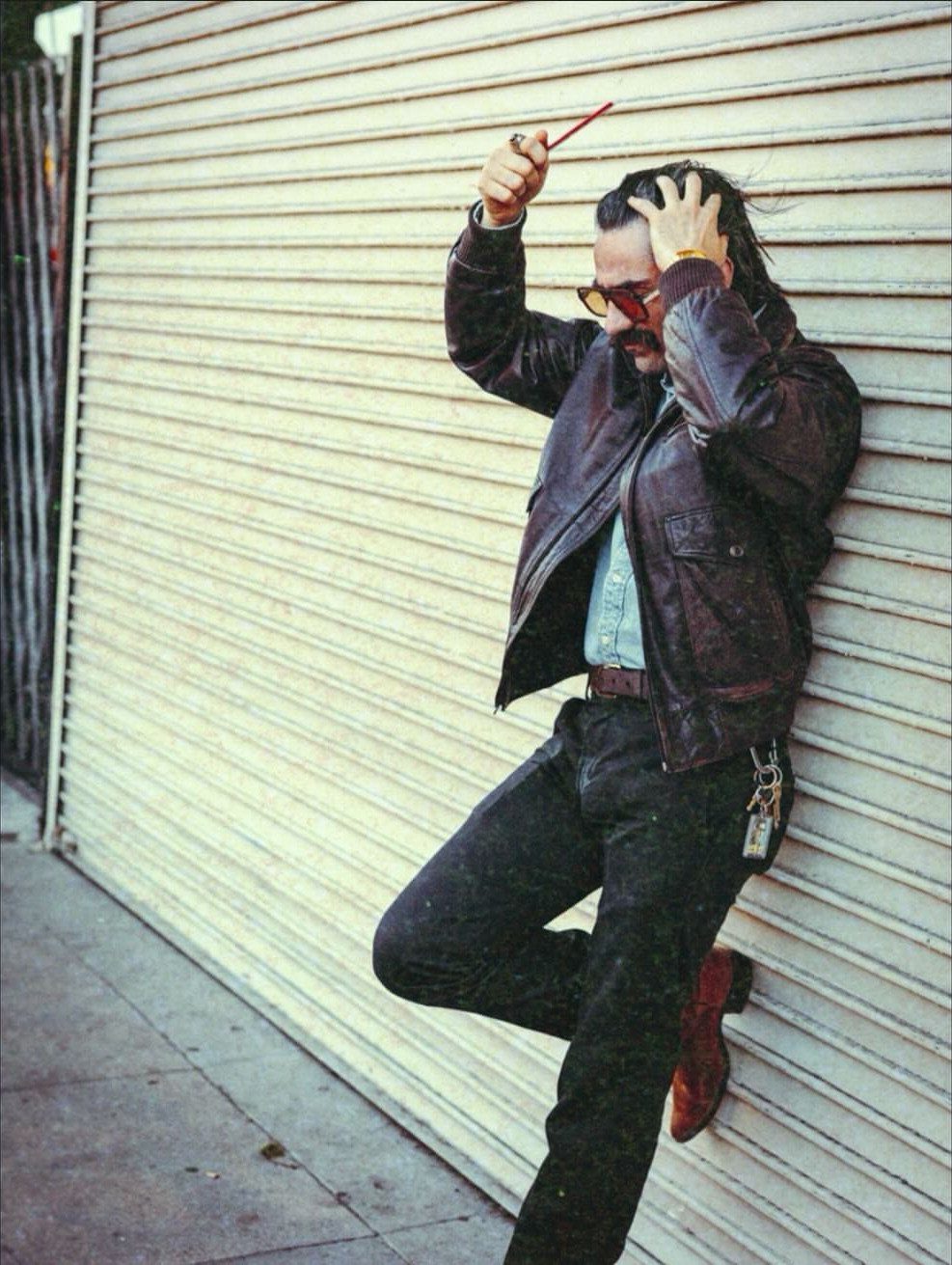 10 Images of 70's Men's Fashion from Flares to Fur Coats 10 Man in brown leather jacket and sunglasses leaning against a white corrugated wall.