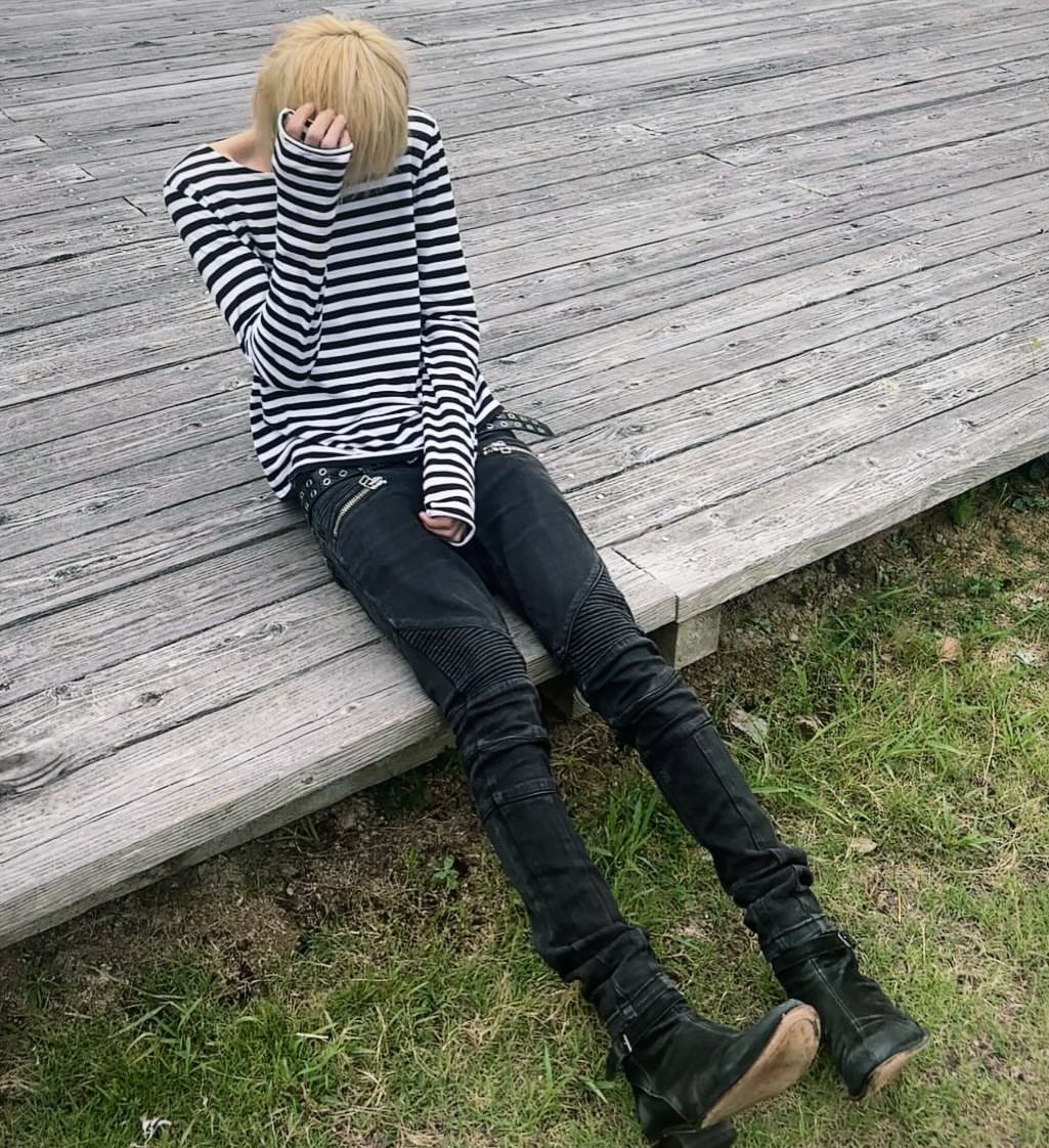 Person in striped shirt and slim black jeans sitting on a wooden deck.