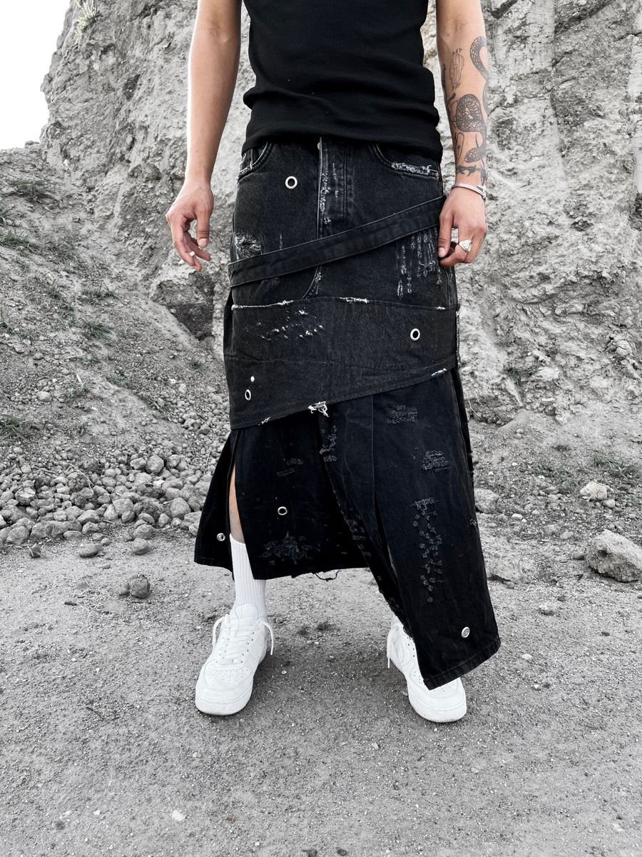 Person wearing a deconstructed black denim skirt with straps and white sneakers.