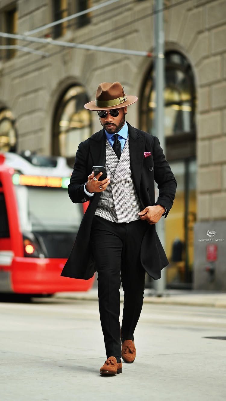 Man in a brown fedora and black overcoat walking on a city street.
