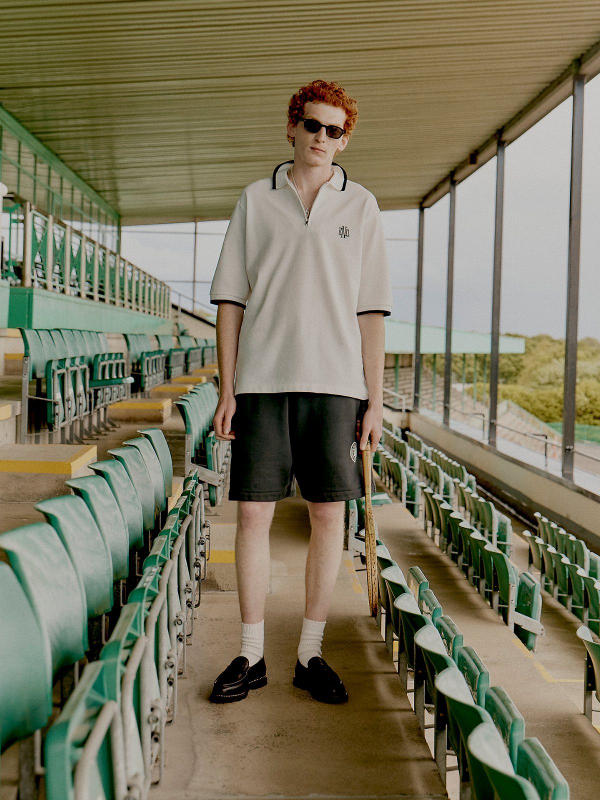 Man with red hair wearing a cream polo and black shorts in a stadium.