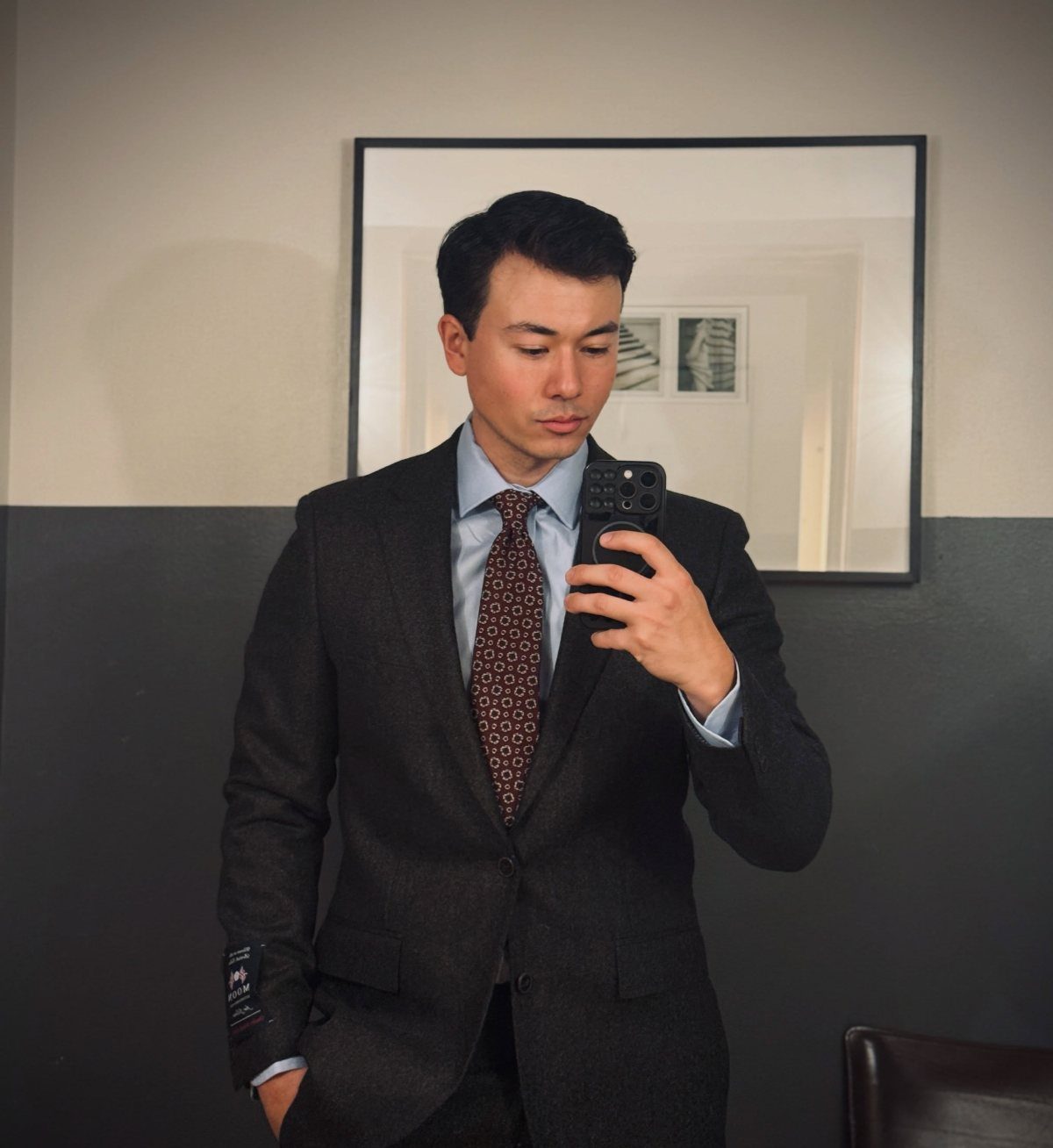 Man in a charcoal grey suit and burgundy tie taking a mirror selfie.
