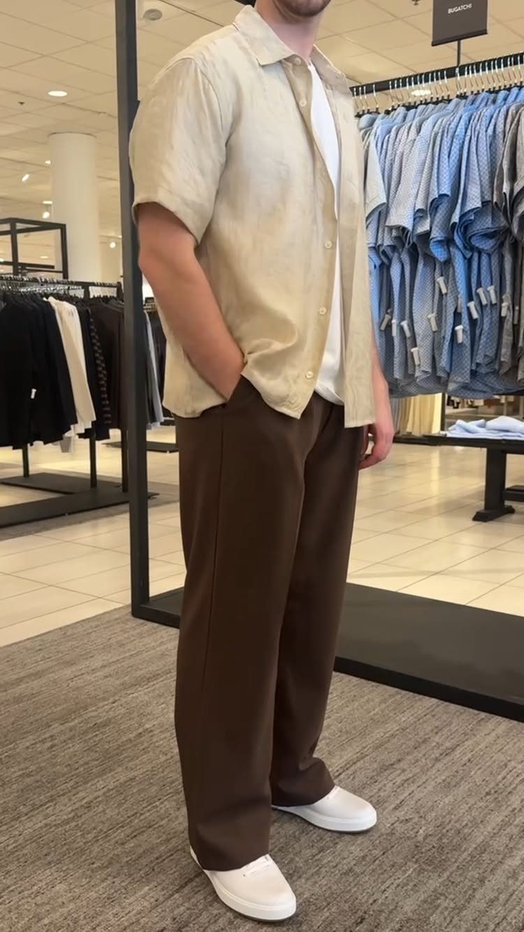 Man wearing a beige button-down shirt and brown trousers in a clothing store.