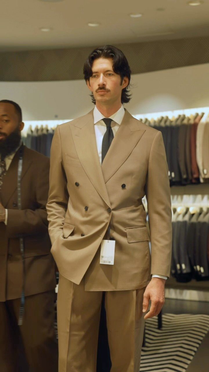 Man wearing a tan double-breasted suit and tie in a clothing store.