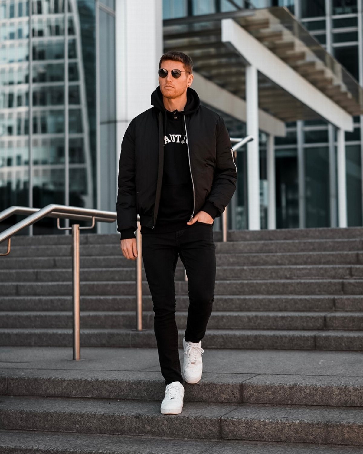 Man in black bomber jacket and black jeans walking down stone steps.