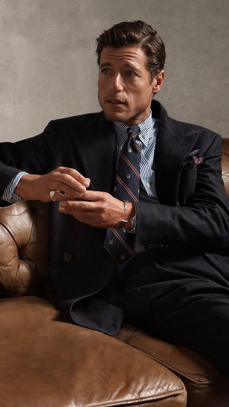Man in a navy suit and striped tie sitting on a leather sofa.