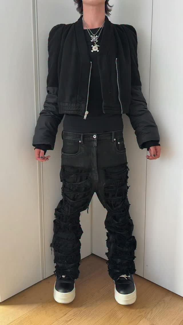 Person wearing a cropped black bomber jacket and heavily distressed black denim jeans.