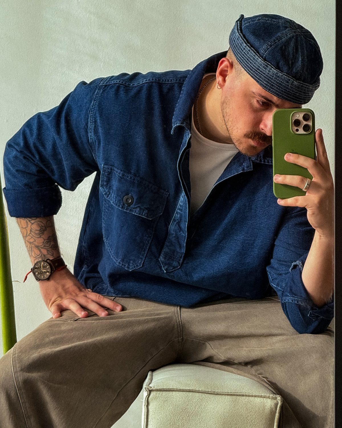 Man in blue denim shirt and cap taking a mirror selfie.