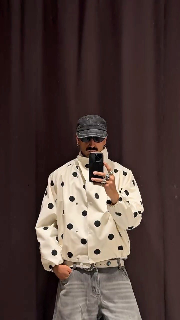 Man in a white polka dot jacket and grey cap posing for a selfie.