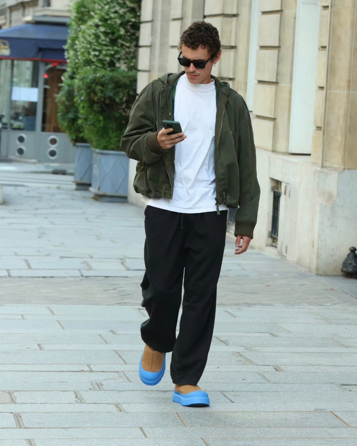 Man in olive jacket and black trousers wearing bright blue Ugg clogs.