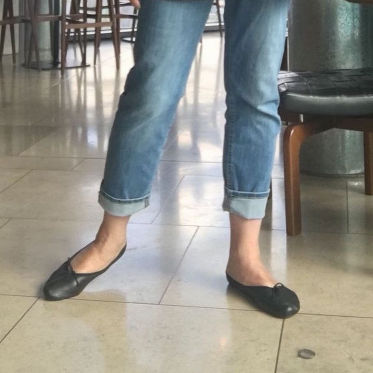 Person wearing cuffed blue jeans and black leather ballet flats on tiled floor