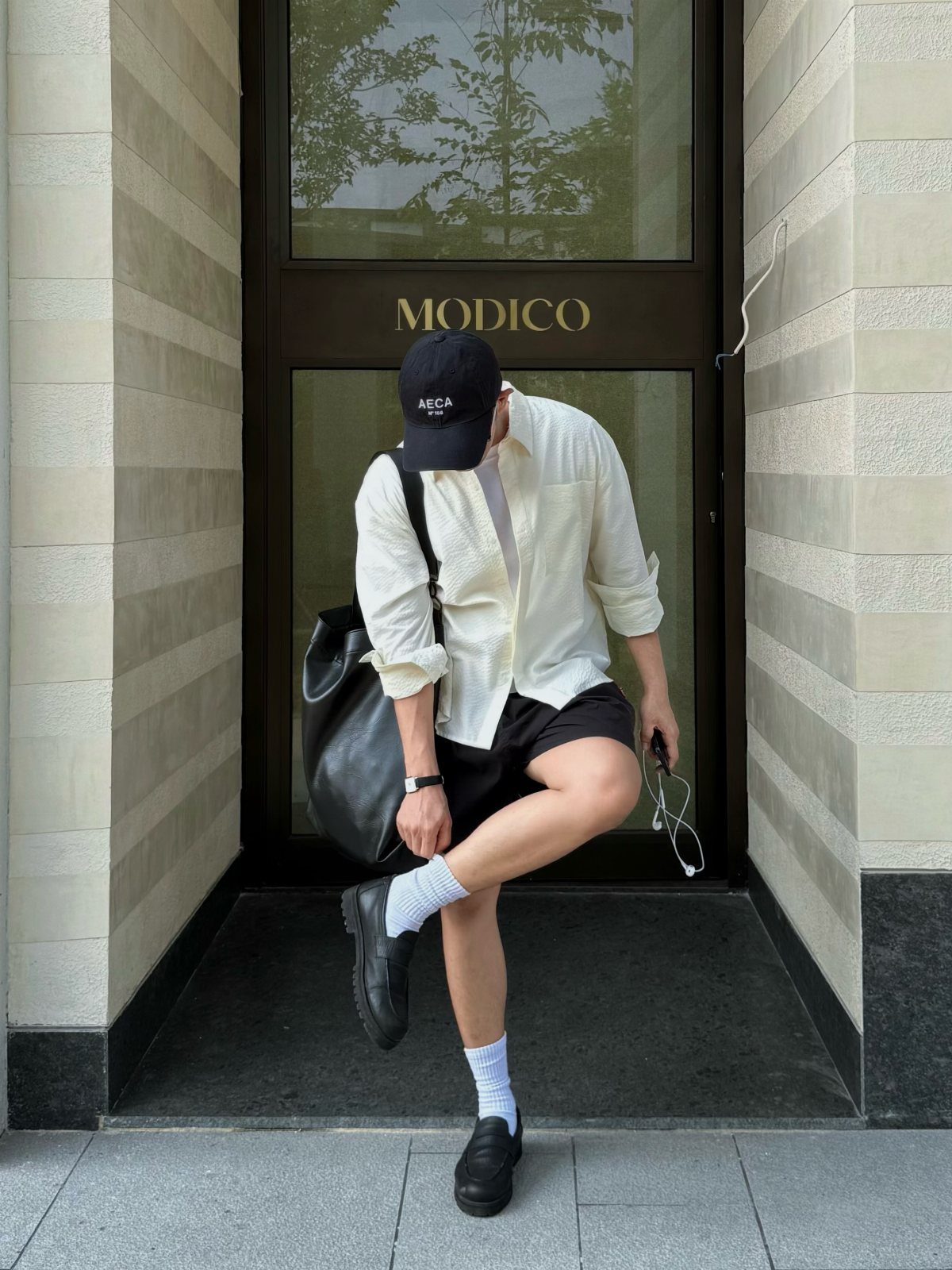Man in white shirt and black shorts wearing black ballet flats and white socks.