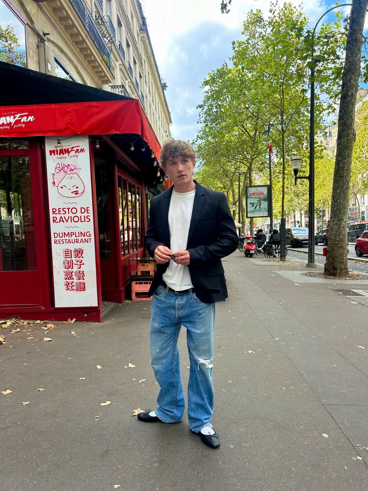 Man in a black blazer and baggy jeans wearing black ballet flats on a sidewalk