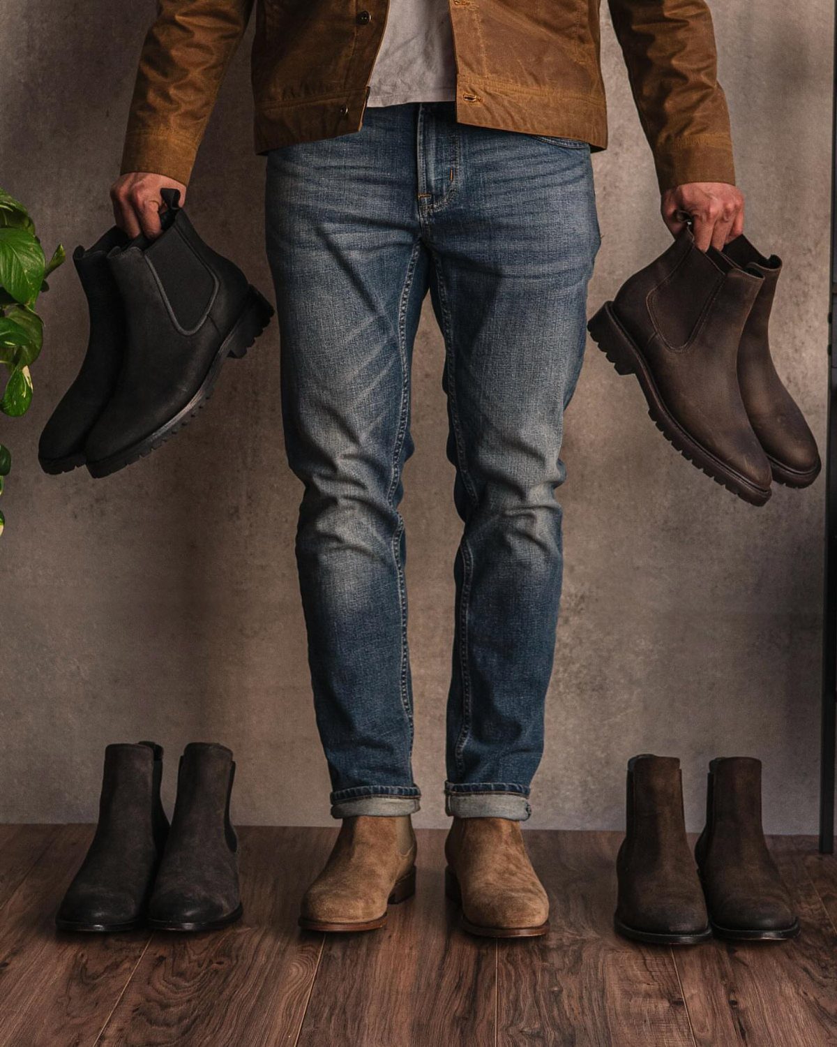Man in brown jacket and blue jeans wearing tan suede Chelsea boots.