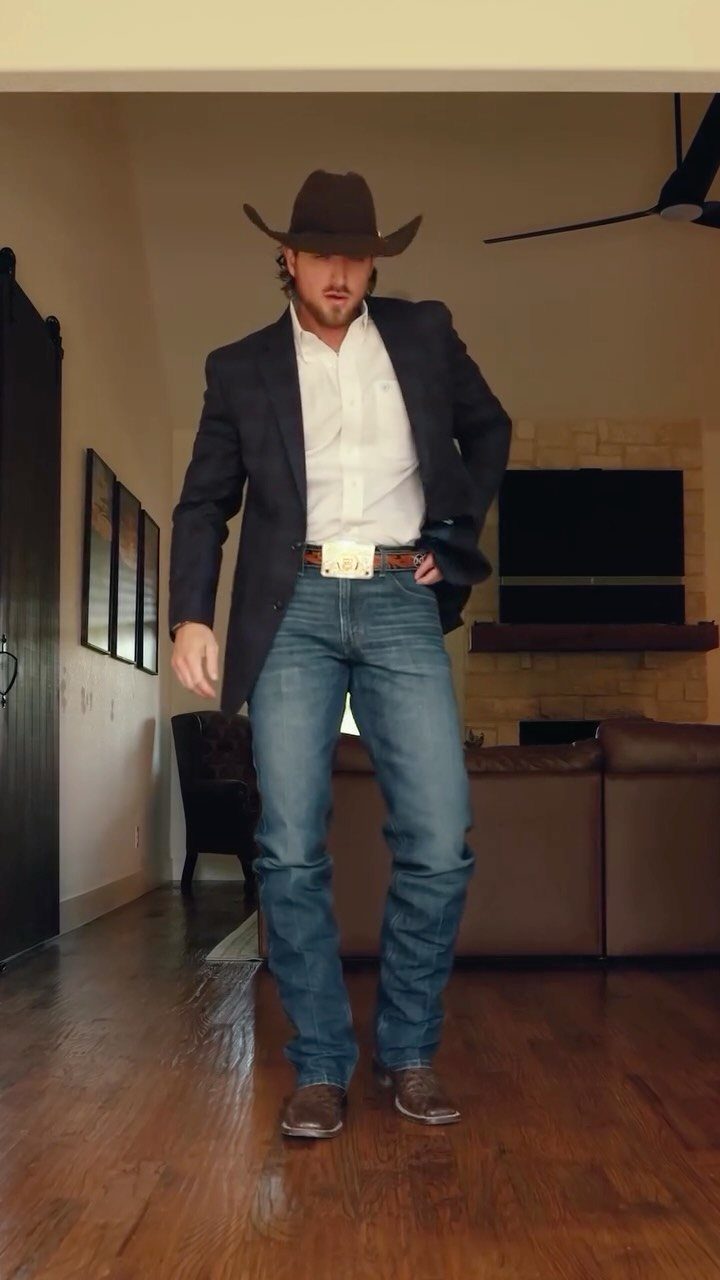 Man in cowboy hat, navy blazer, blue jeans, and boots in a living room.