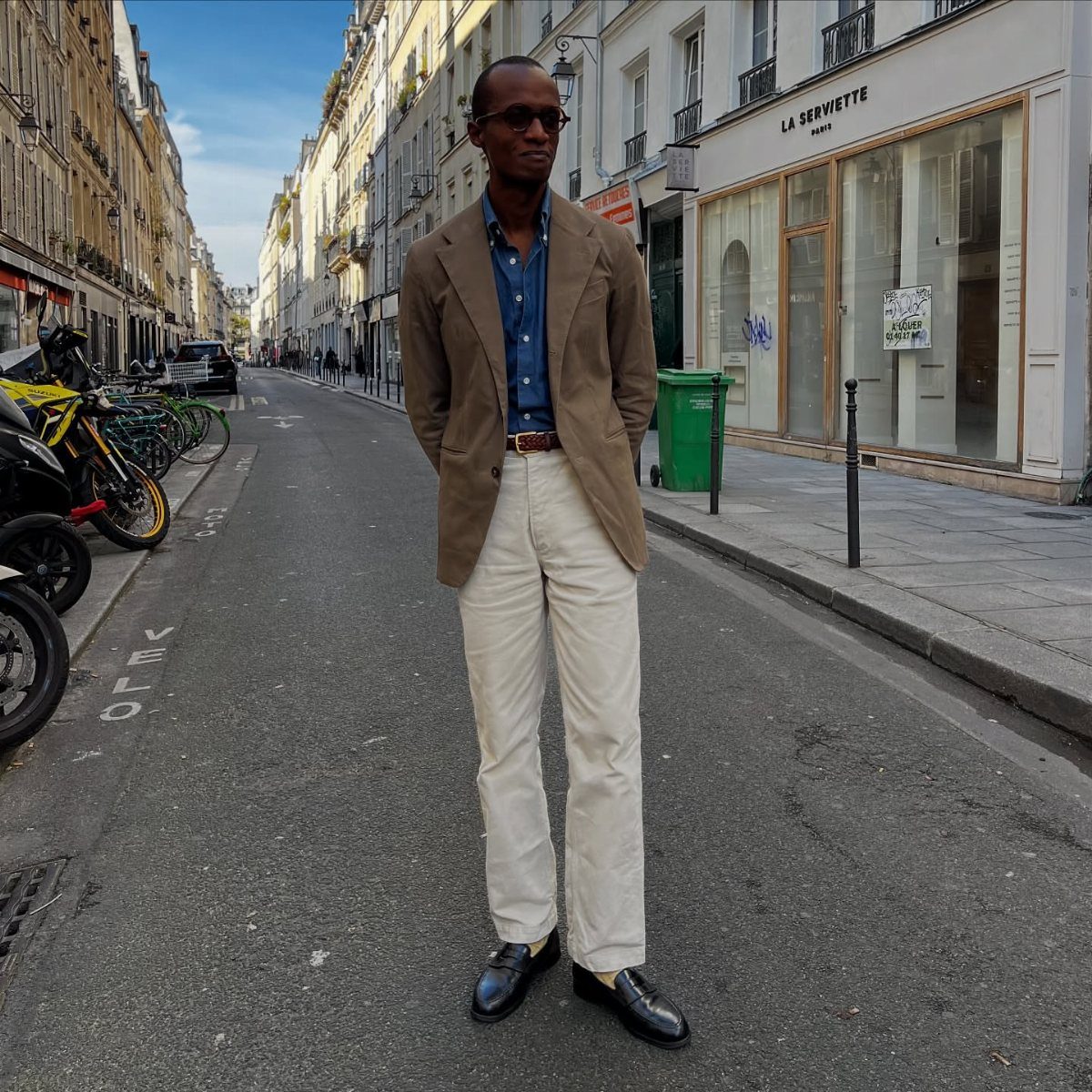 Man wearing a brown blazer and beige trousers on a city street.