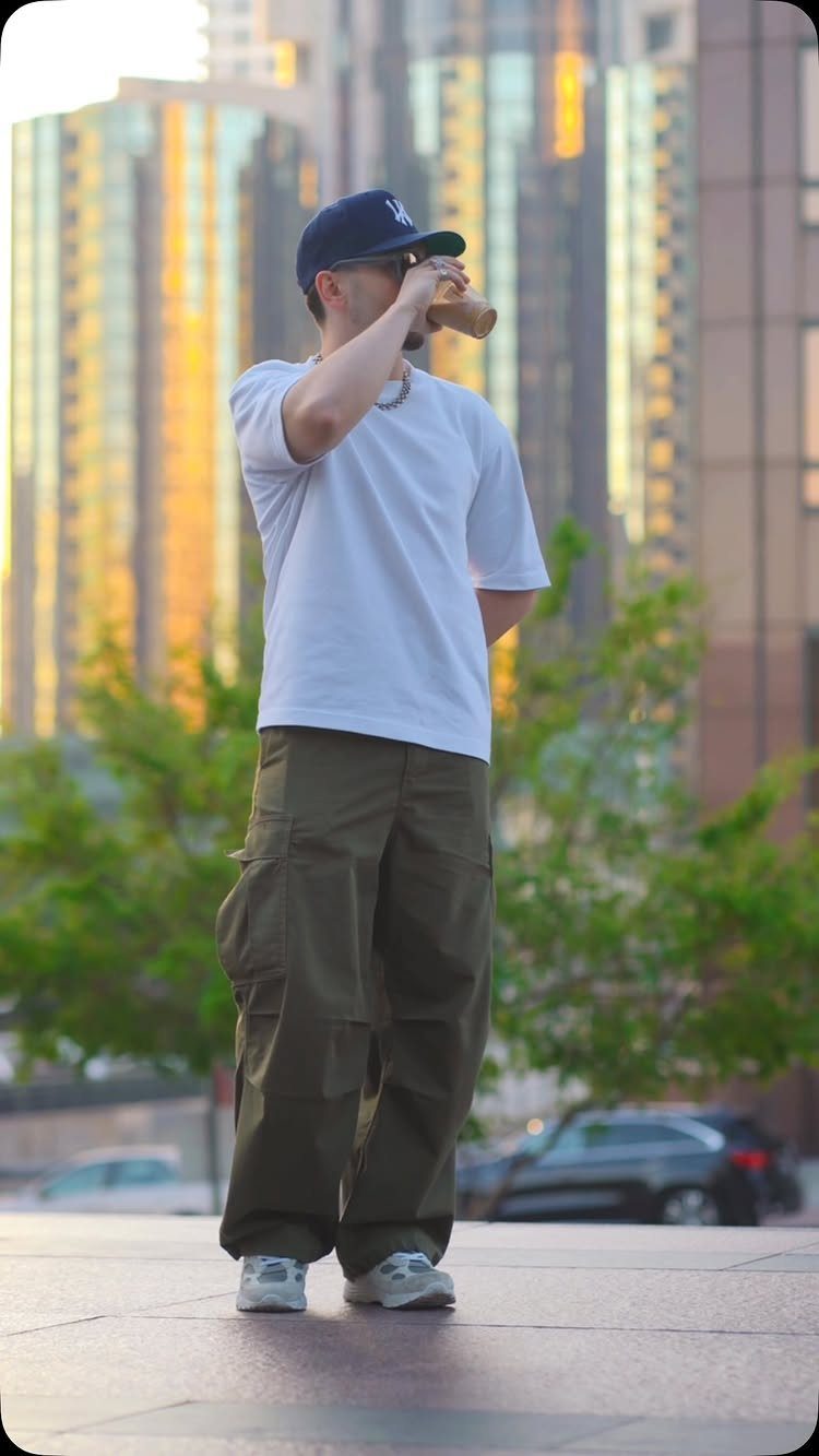 Man in white t-shirt and olive cargo pants standing in a city environment.