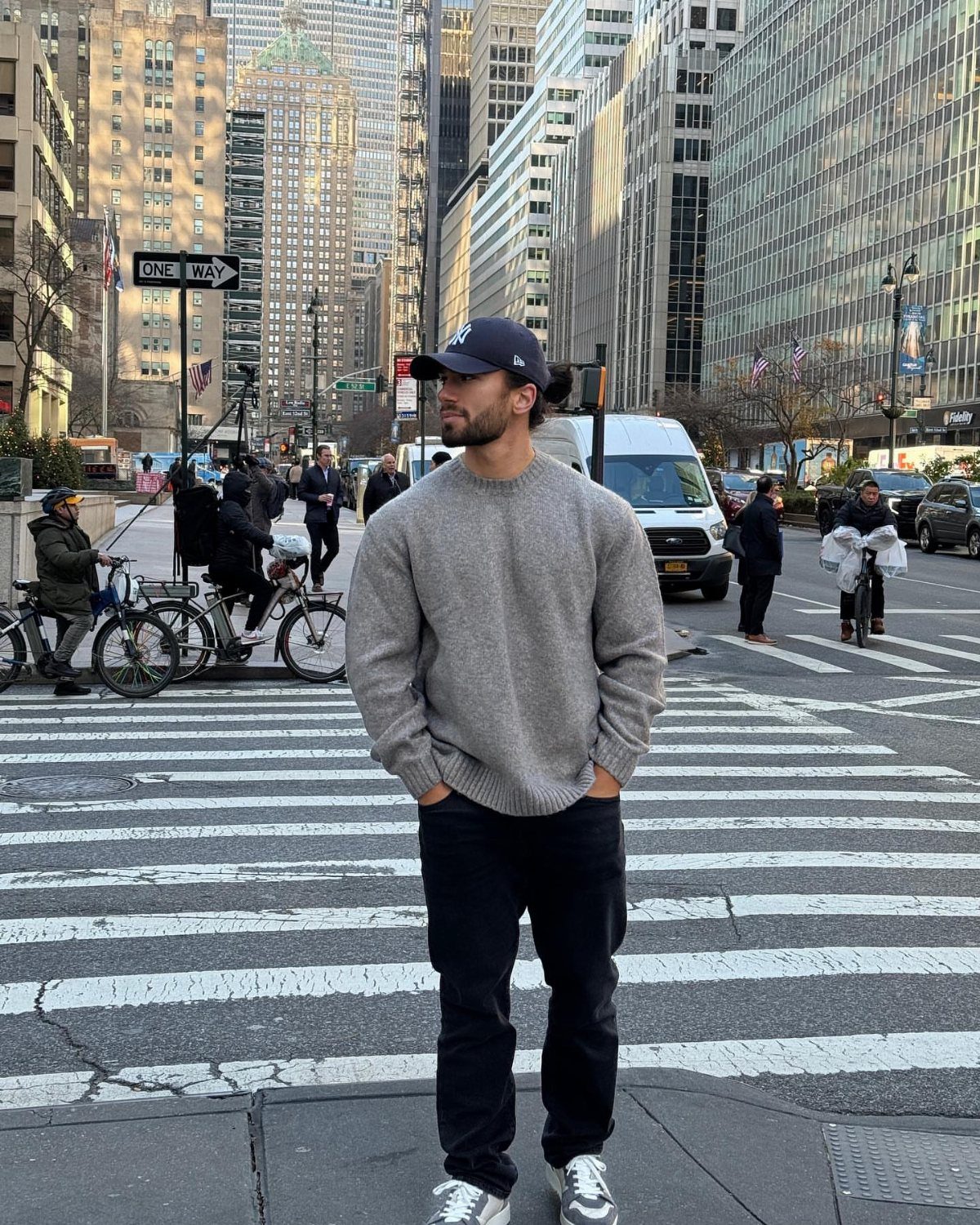 Man in oversized grey sweater and black trousers standing on a city street.