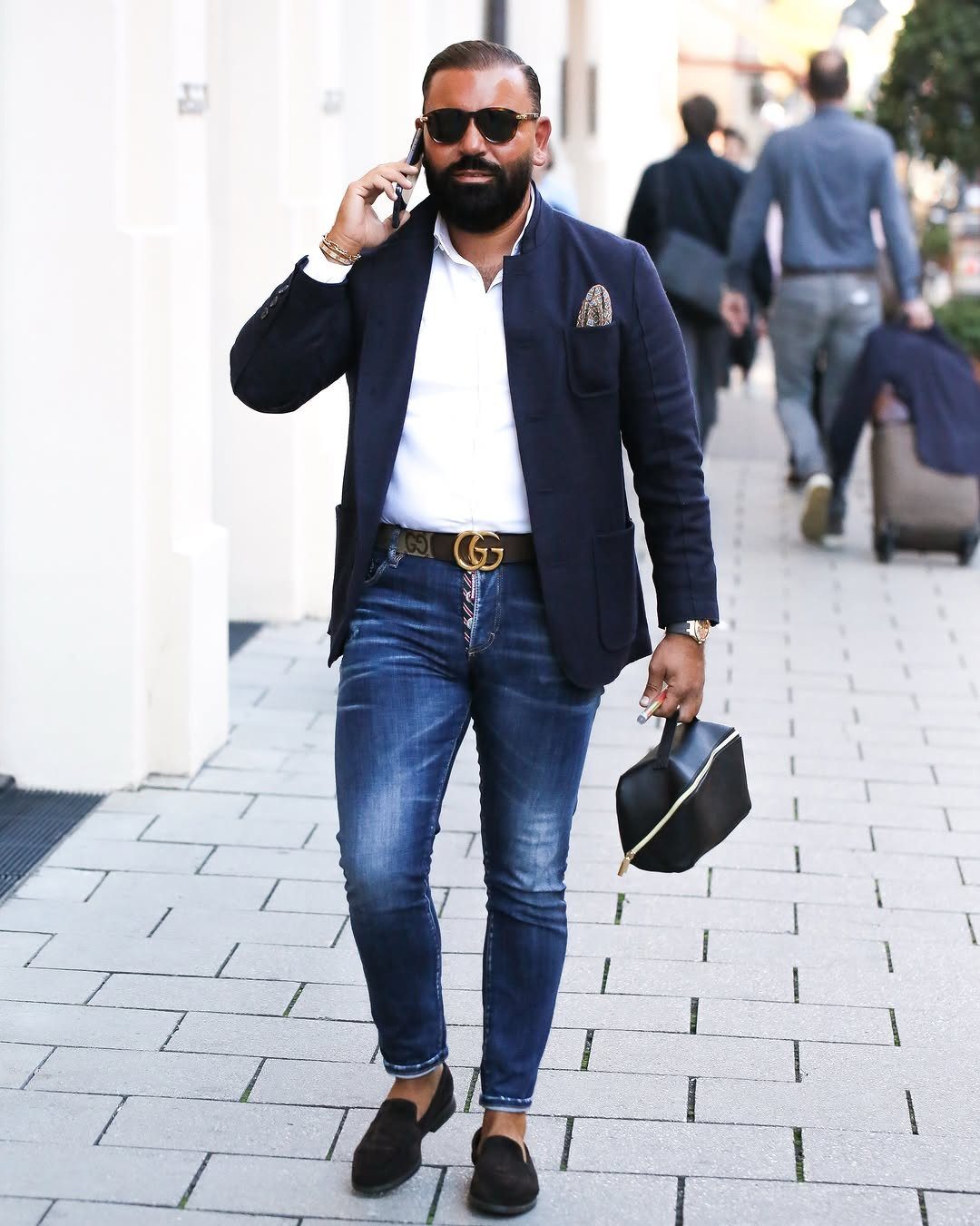 Man in navy blazer, white shirt, and blue jeans walking on a city street.