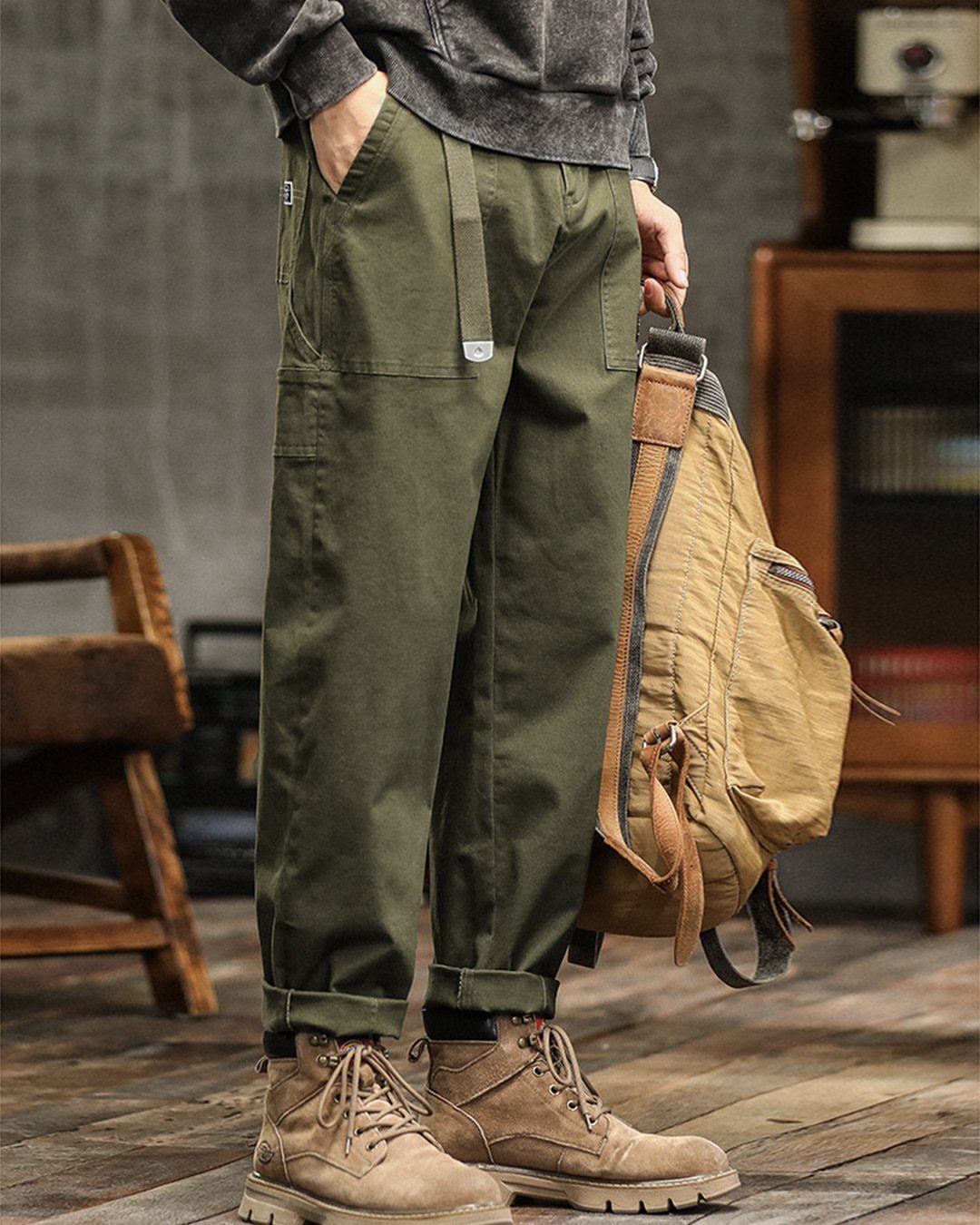 Man wearing olive green cargo pants, tan boots, and carrying a canvas backpack.