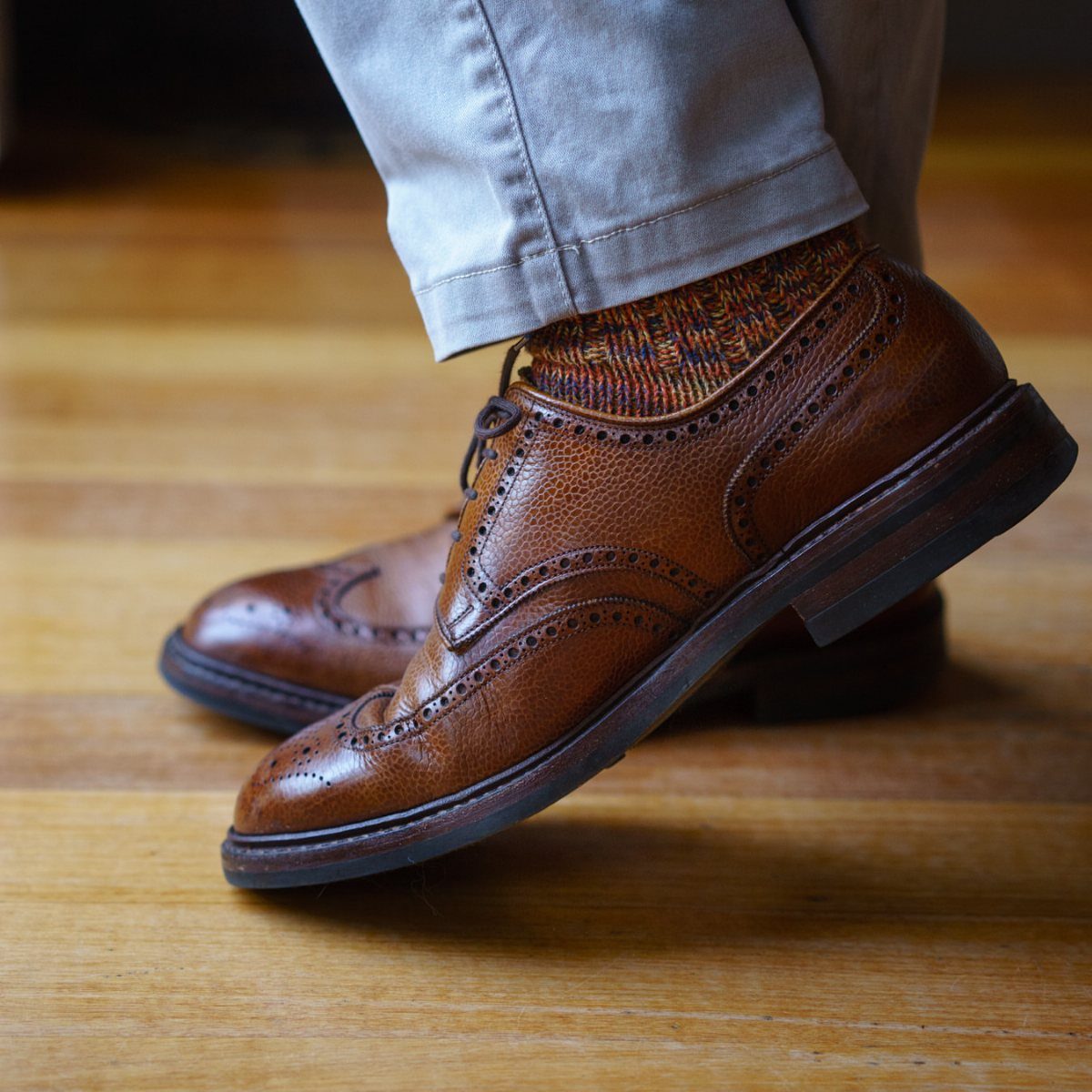 Brown leather wingtip brogue shoes and patterned socks on a wooden floor.