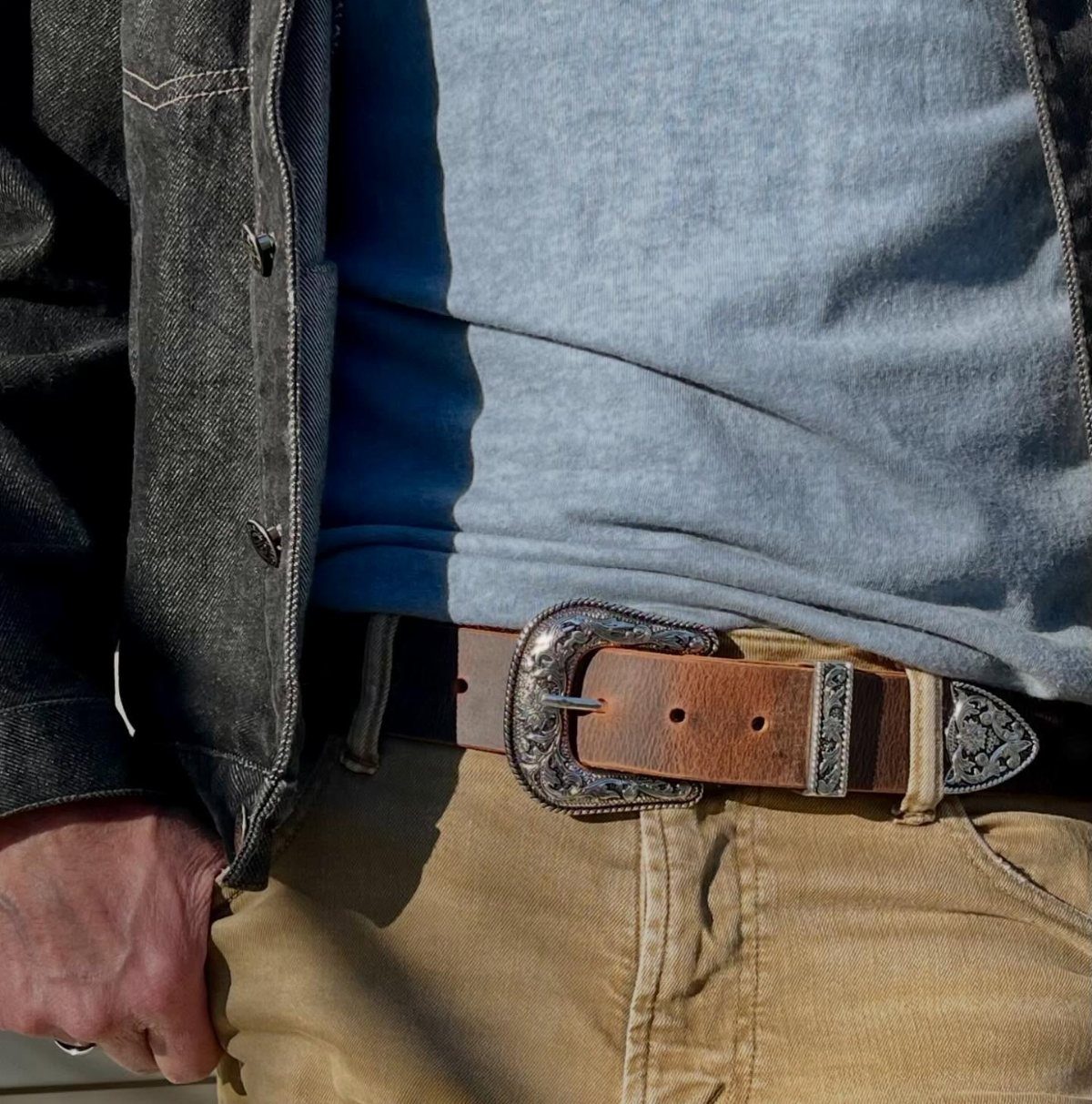 Man wearing a brown leather belt with a large ornate silver western buckle.