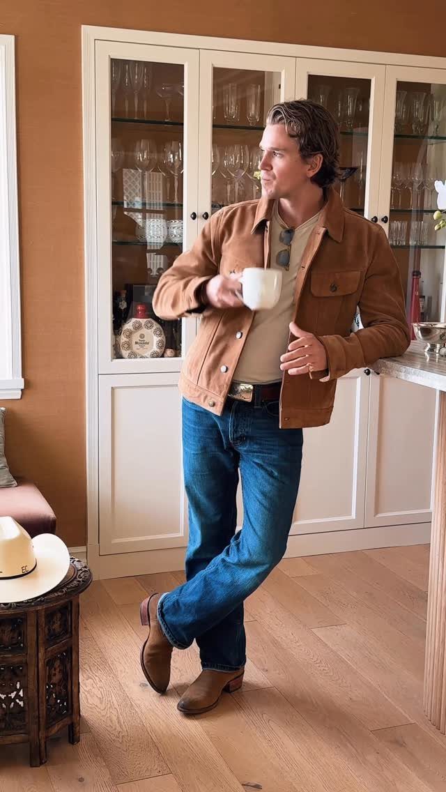 Man wearing a brown suede trucker jacket and blue jeans holding a white mug.