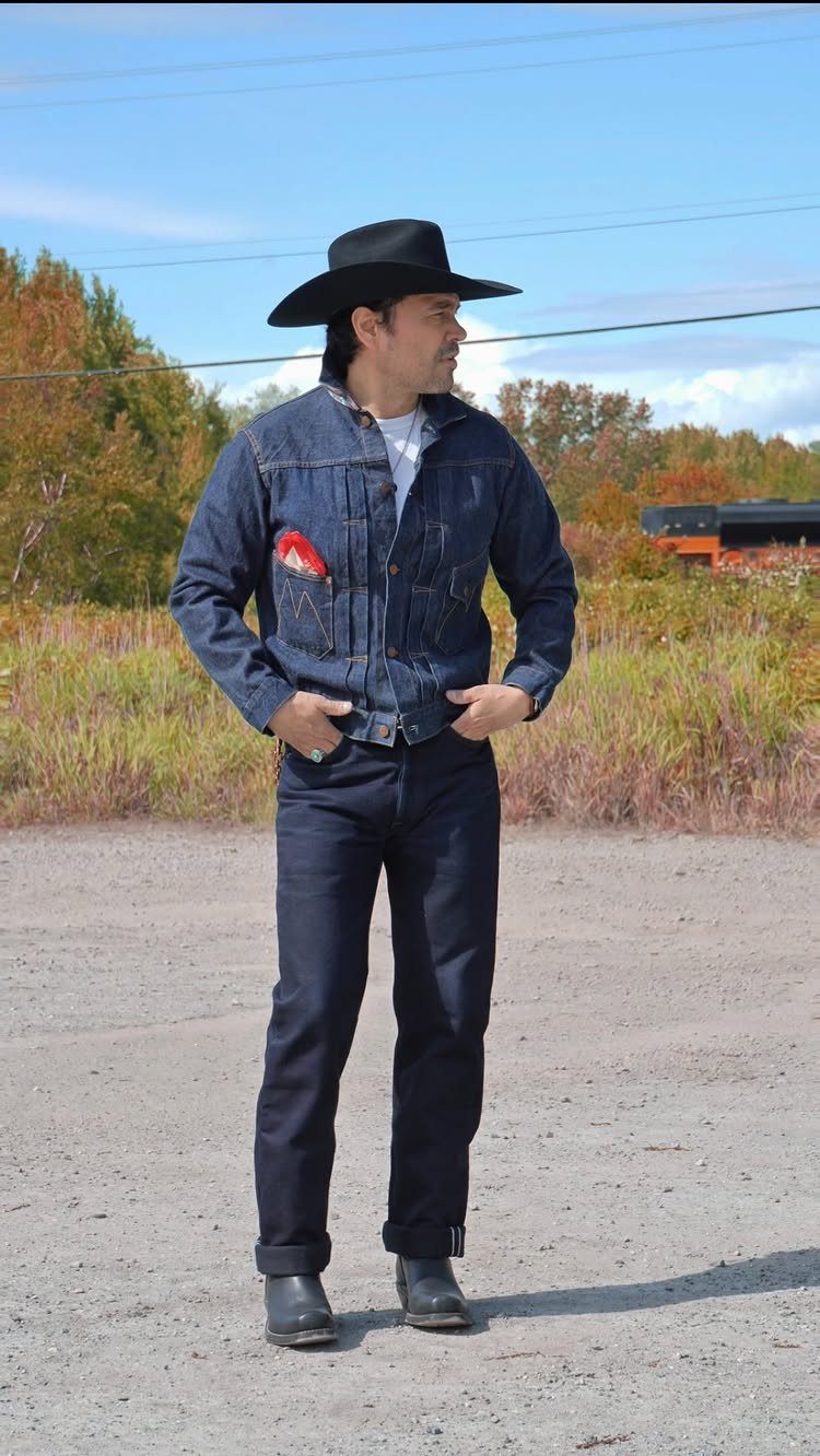 Man wearing a dark blue denim jacket and jeans with a black cowboy hat