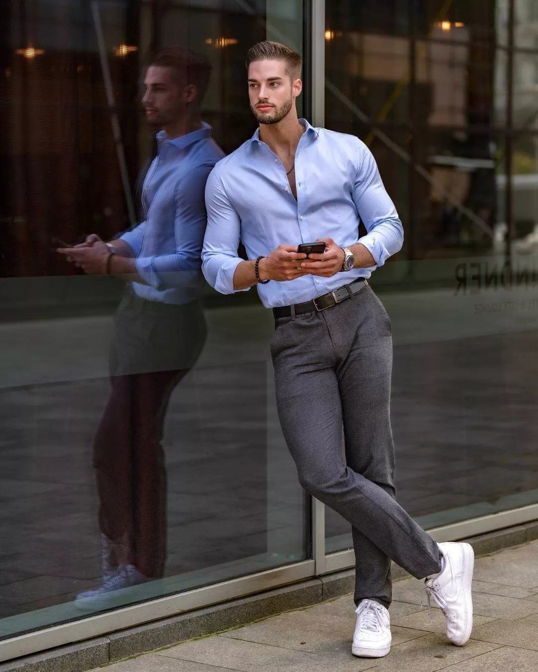 Man in light blue shirt and grey trousers leaning against a glass window