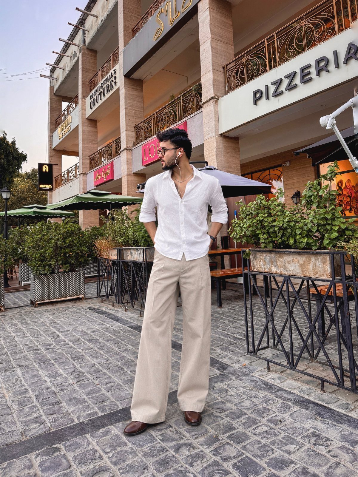 Man in white shirt and beige wide-leg trousers posing on a city street.