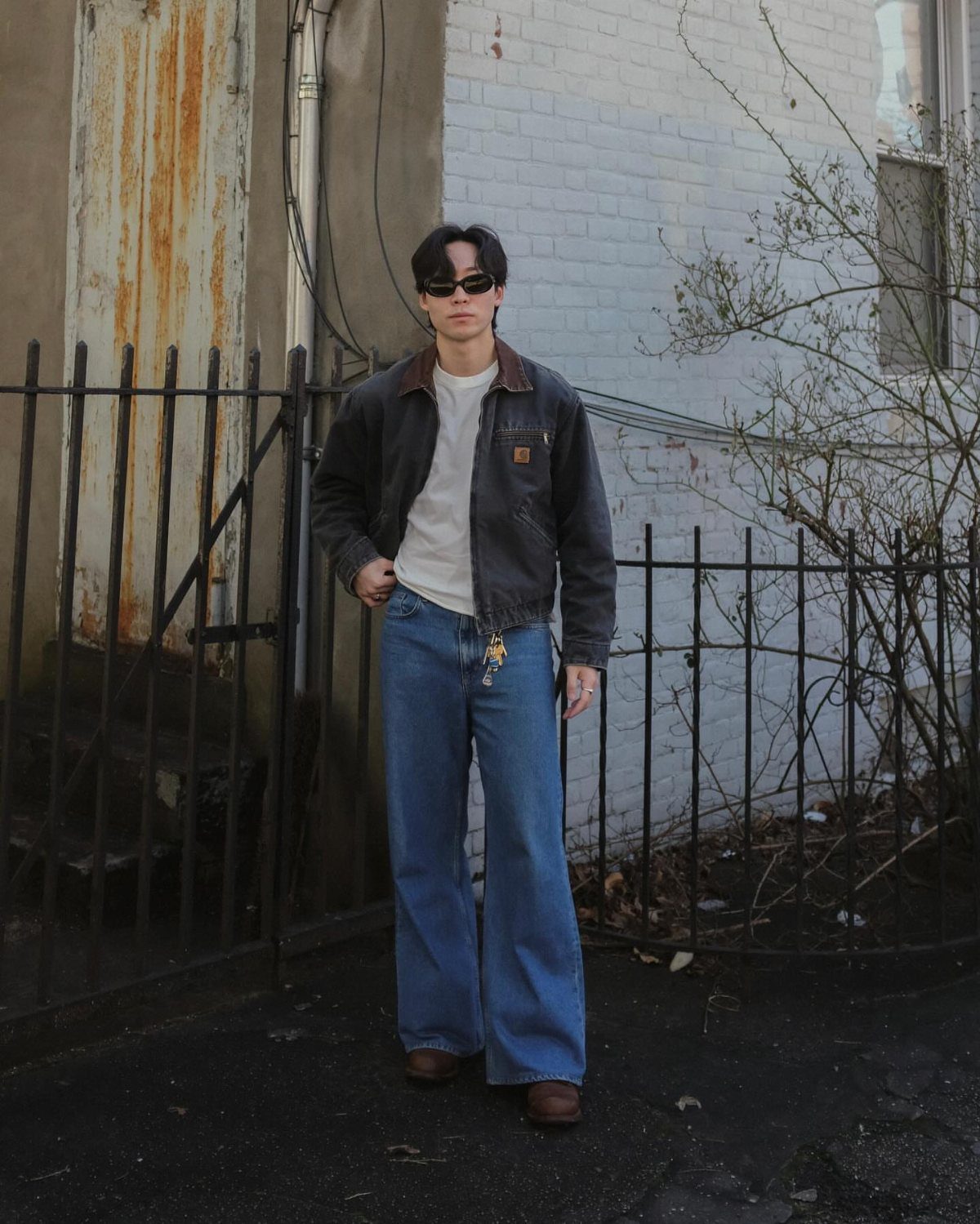 Man in a simple outfit with a grey jacket and wide blue jeans.