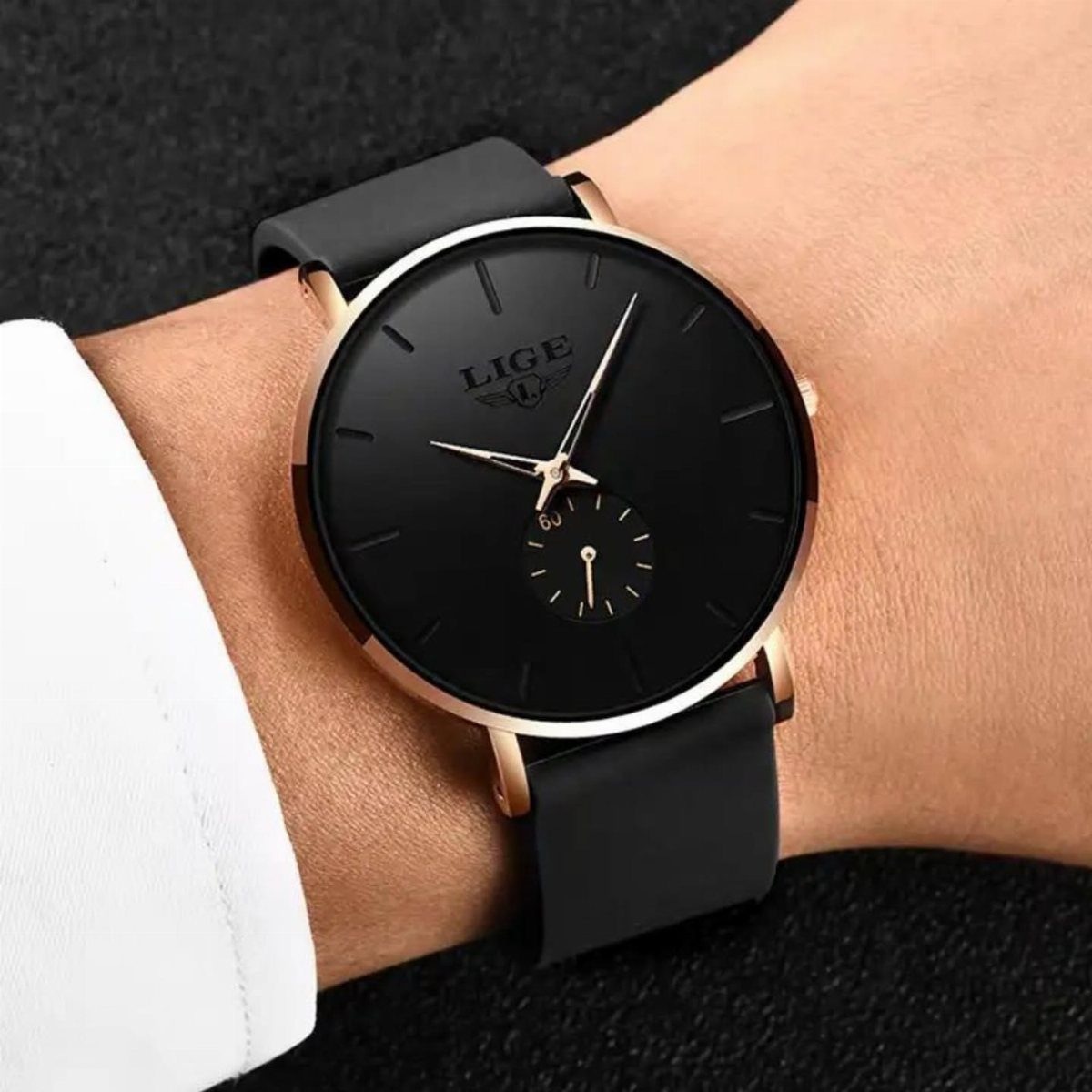 Minimalist black watch with rose gold case on a wrist with white cuff.