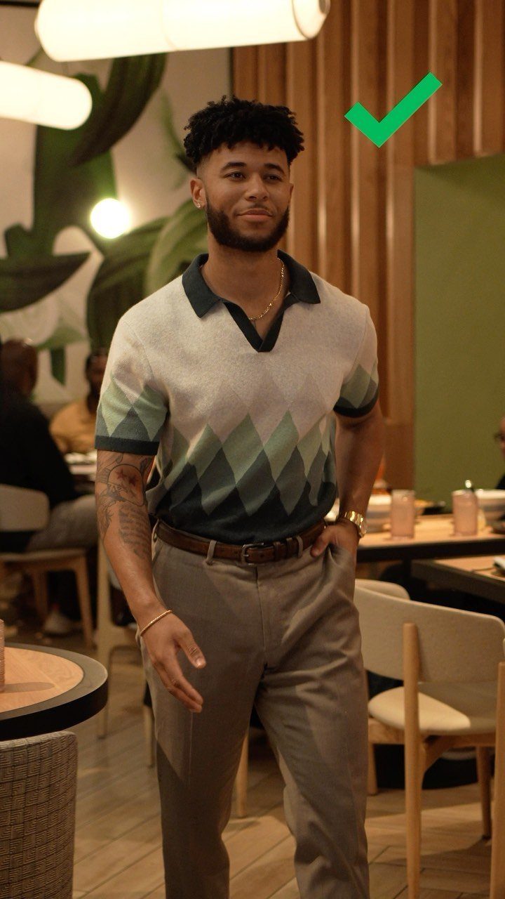 Man wearing a patterned knit polo shirt and brown trousers in a cafe.