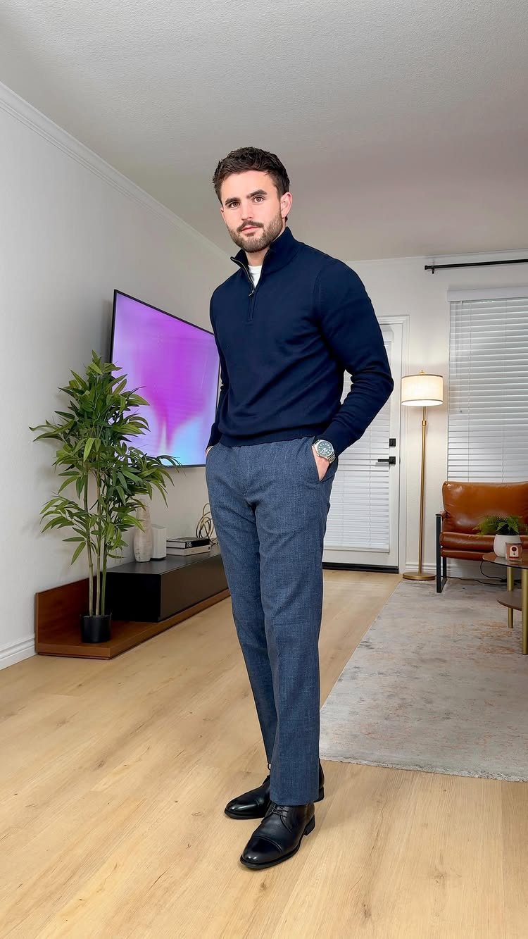 Man wearing a navy quarter-zip sweater and grey trousers in a modern living room.