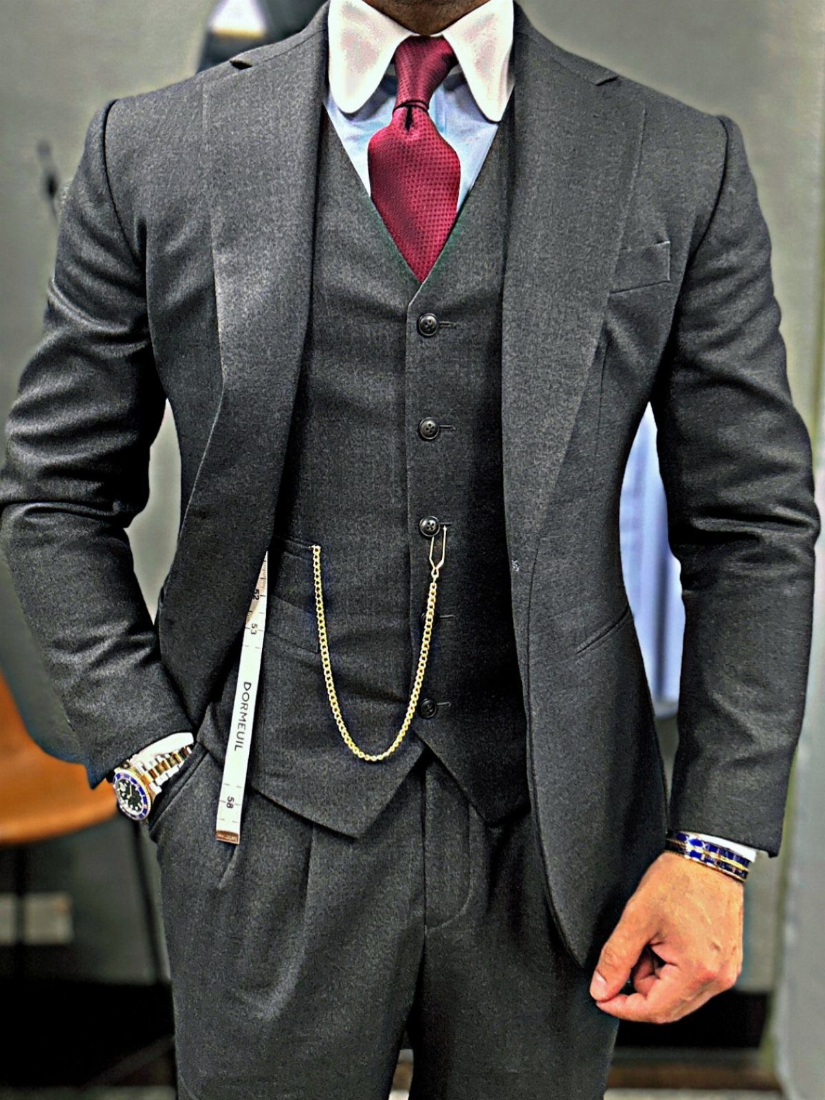 Man wearing a charcoal grey three-piece suit with a red tie and gold chain.