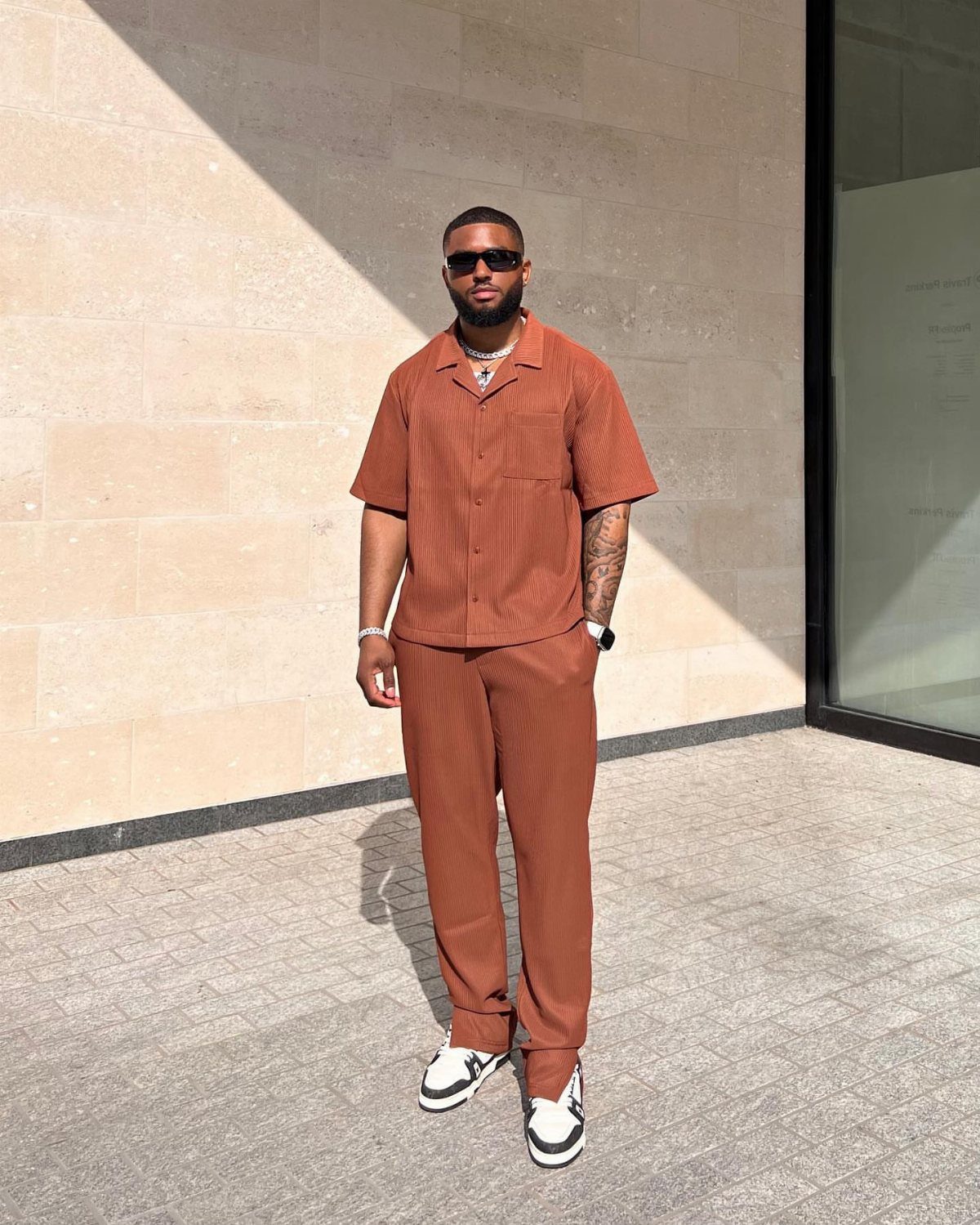 Man wearing a brown boxy shirt and matching trousers with white sneakers.